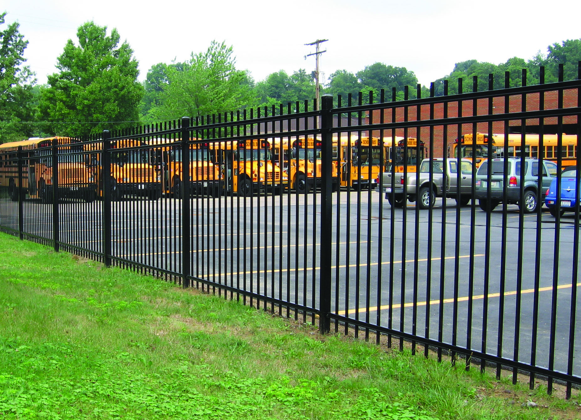 Black ornamental metal perimeter fence surrounding a school parking area with buses.